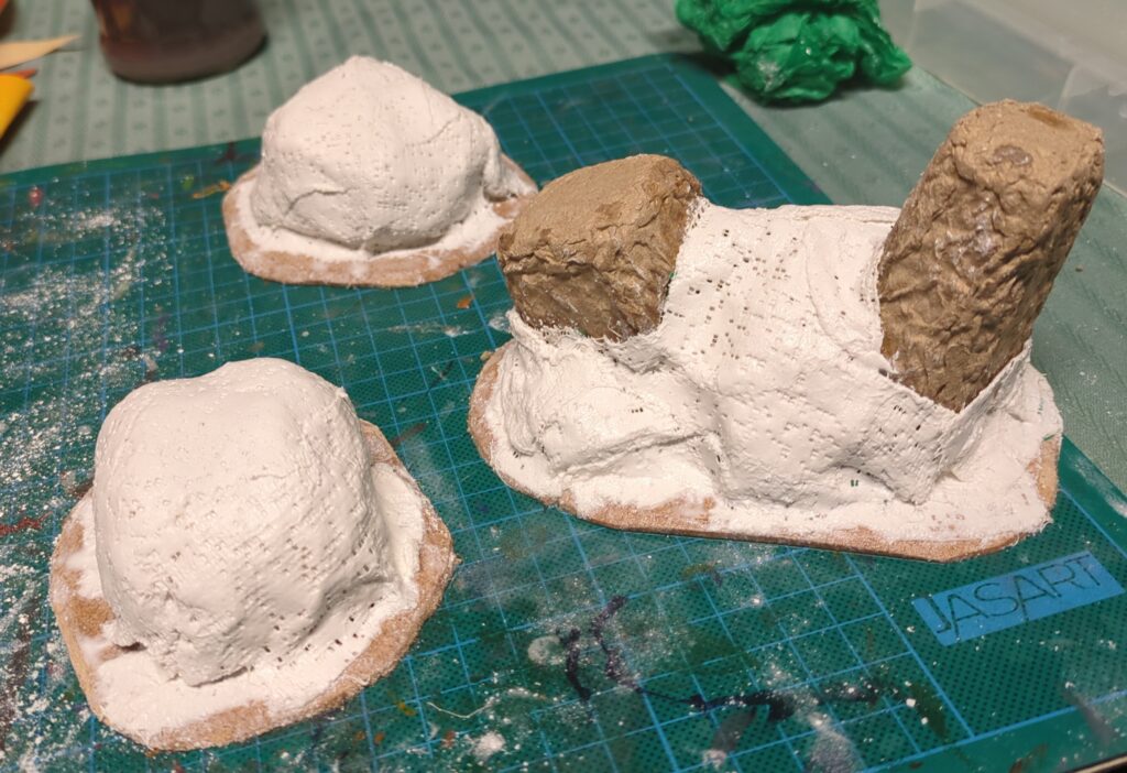 Several smaller plaster hills are glued to MDF bases, each maybe 3-4 inches in length (sized to make for good scatter terrain). One has a few bits of cardboard packaging sticking out of it, as if they were ruins of some kind.