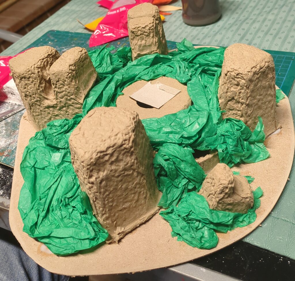 Some cardboard packaging attached to a simple MDF base. Green crepe paper has been added to create a basic shape for plastering over.