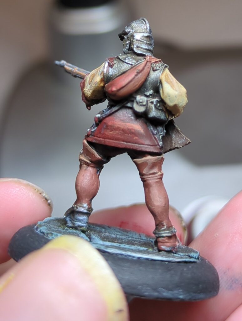 The arquebuser, viewed from the rear, showing the various packs and satchels he's carrying full of supplies.