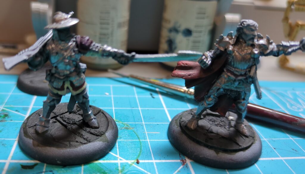Two partially painted Hell Dorado Westerners figurines stand on top of a cyan hobby mat.