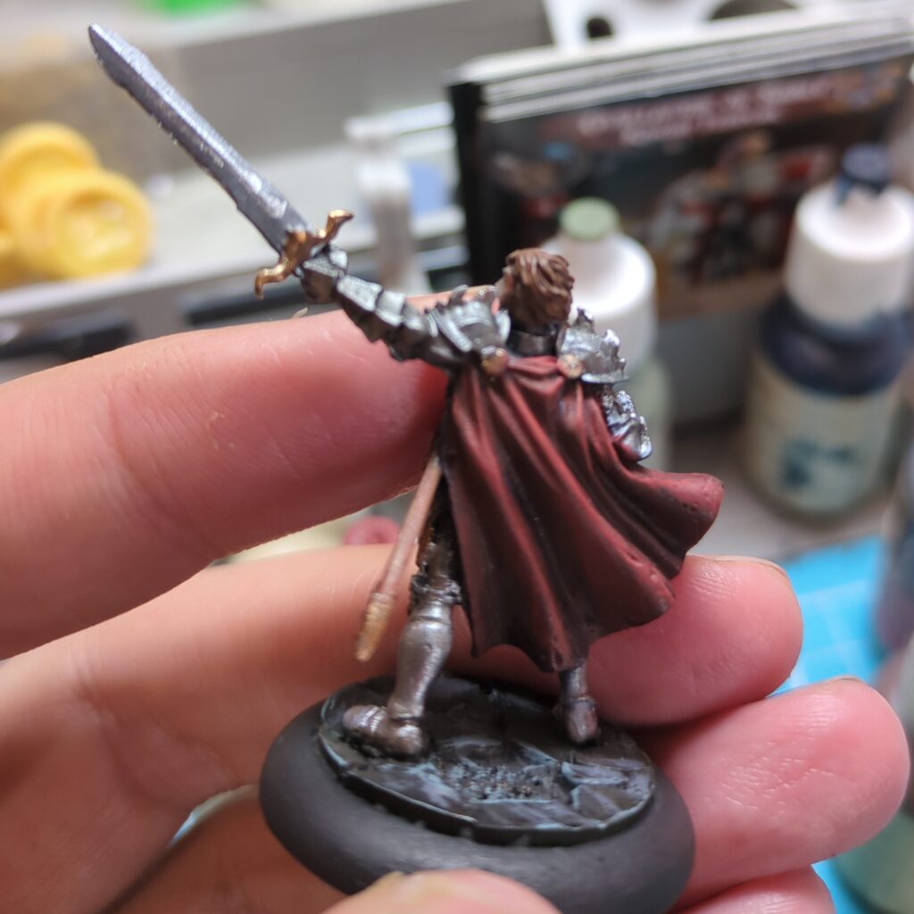 A figurine of a man in plate armour, shown from the back to show off the shadows and highlighting of his flowing red cape.