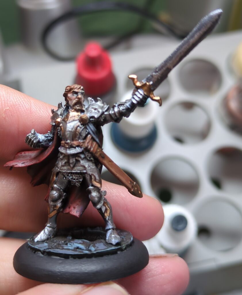 A figurine of a man in ornate plate armour stands, brandishing a sword.