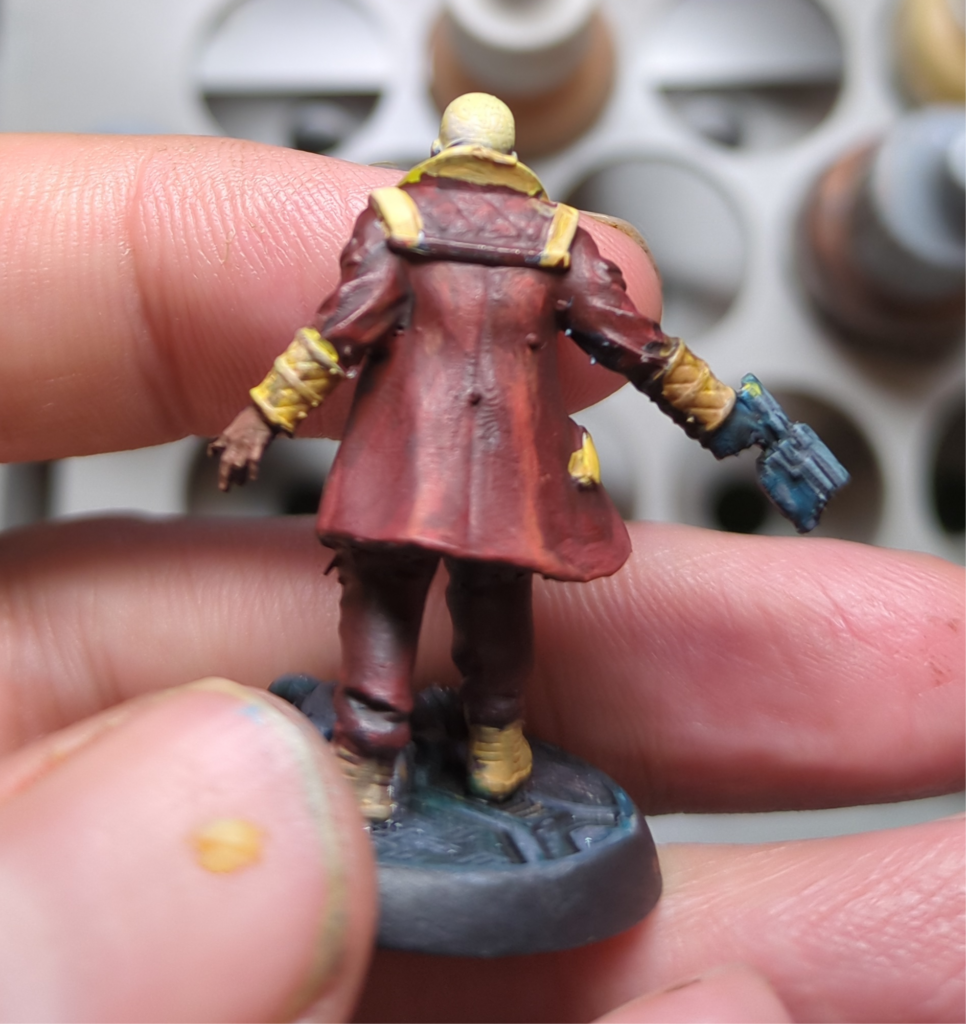 A figurine of a man wearing a red trenchcoat with yellow accents and bracers.