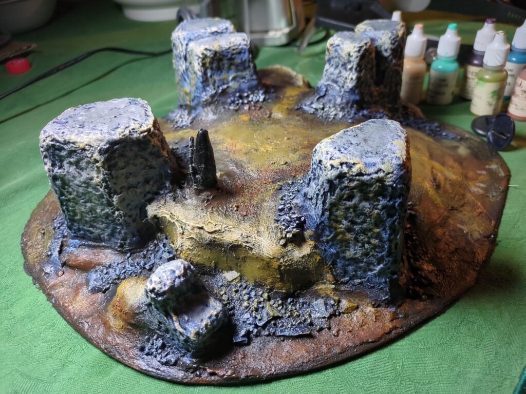 A large painted terrain piece, consisting of four ruined columns spaced around a large hill