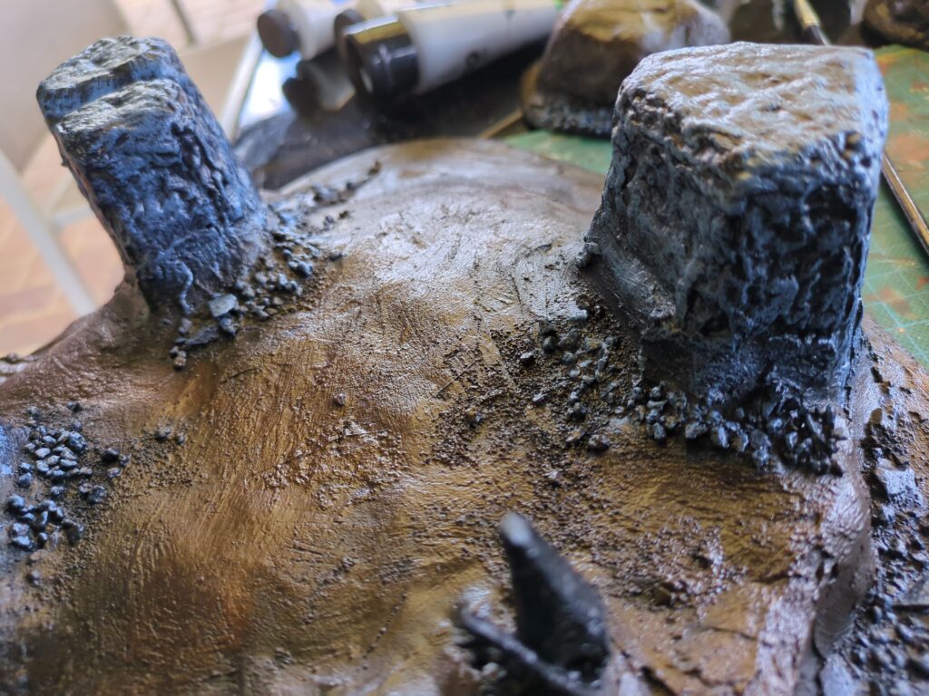 A painted plaster hill with rock monoliths protruding from the earth. A light drybrushing has been applied, giving both the brown earth and the grey stone a bit more shading and depth.