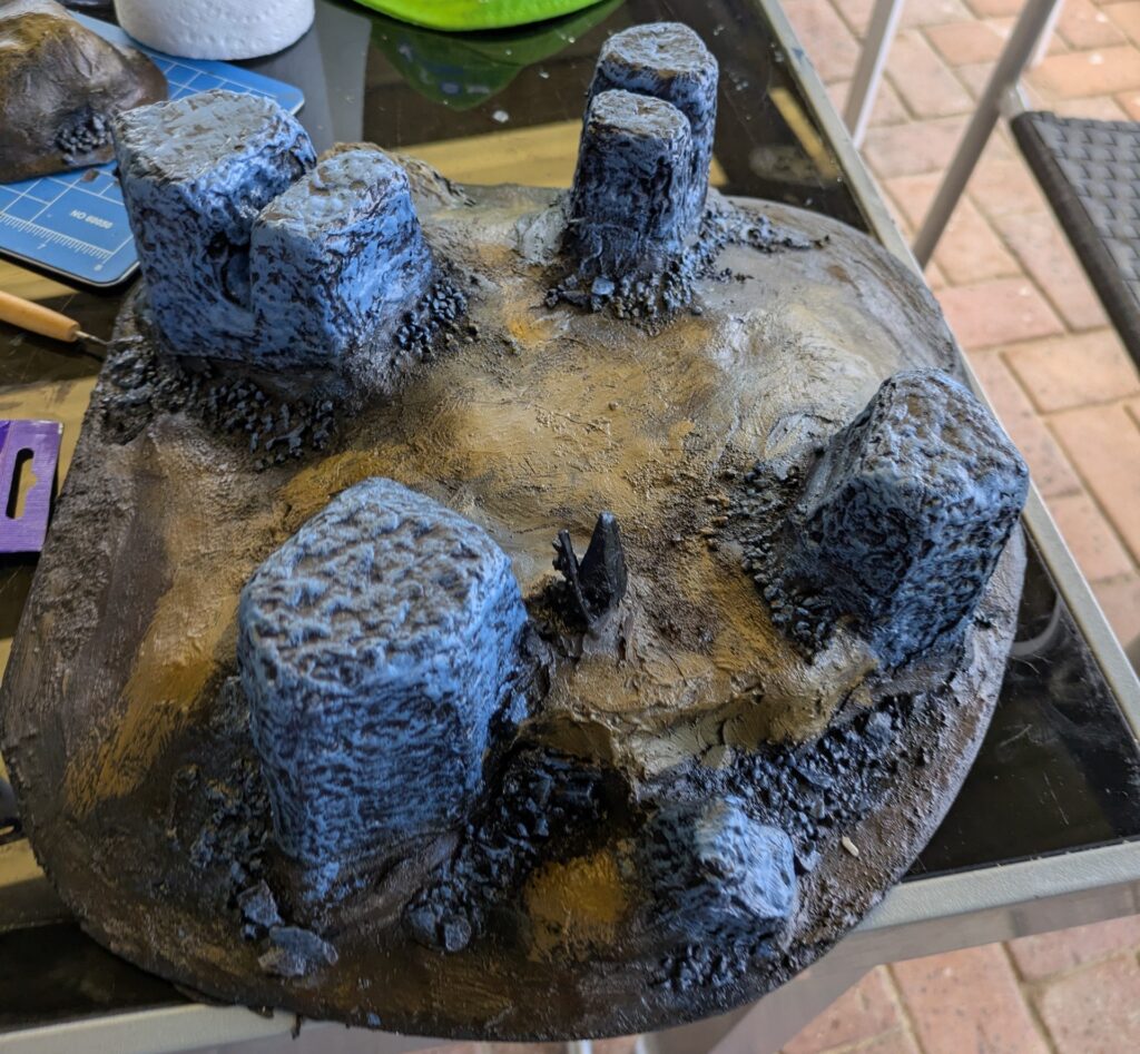 A painted plaster hill with rock monoliths protruding from the earth. The earth has been painted brown and the stone a slate blue-grey, with lighter tones dry-brushed on to provide more shading and depth.