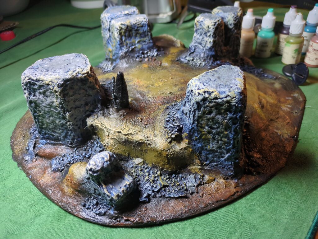 A painted plaster hill with rock monoliths protruding from the earth. The hills are a mixture of browns while the monoliths and rocks are a slate blue-grey.