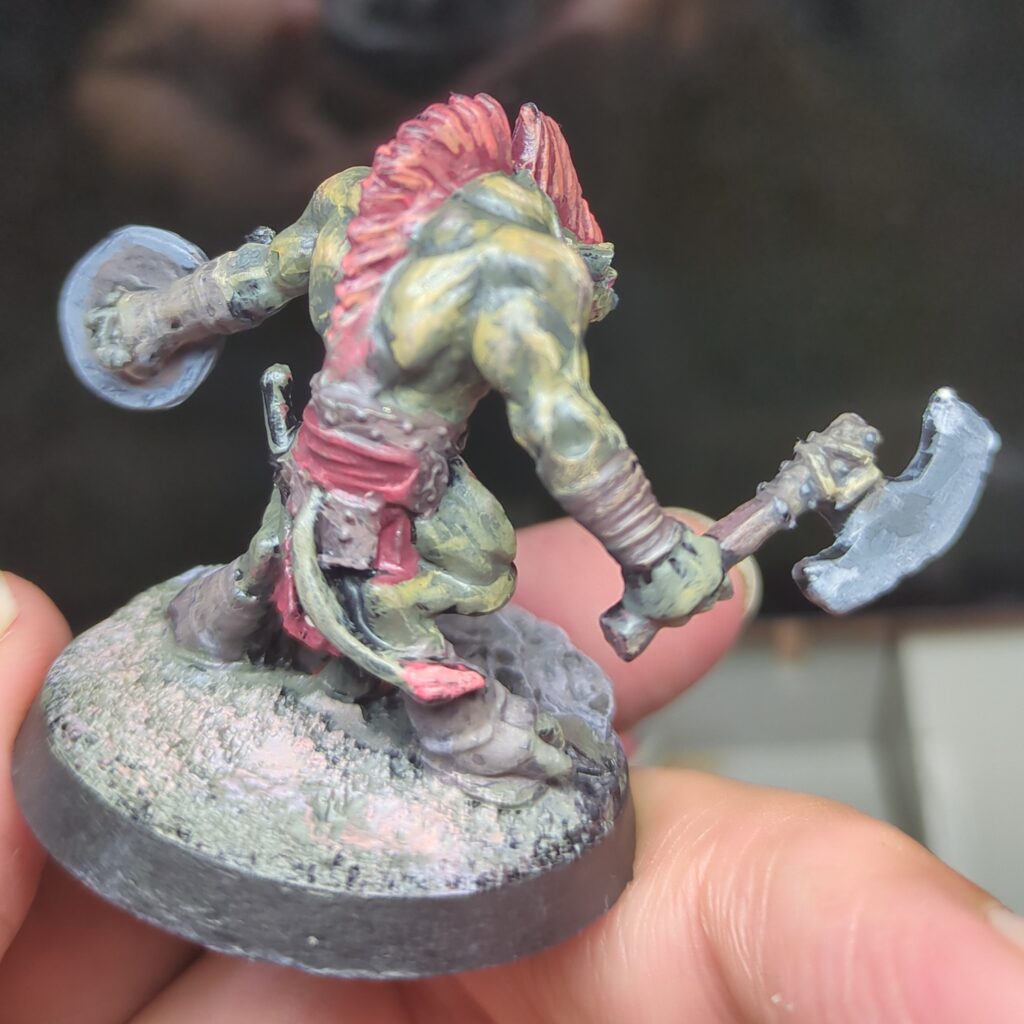 Looking at the back gnoll with greenish yellow skin. His red hair extends down his back to meet his leather belt.