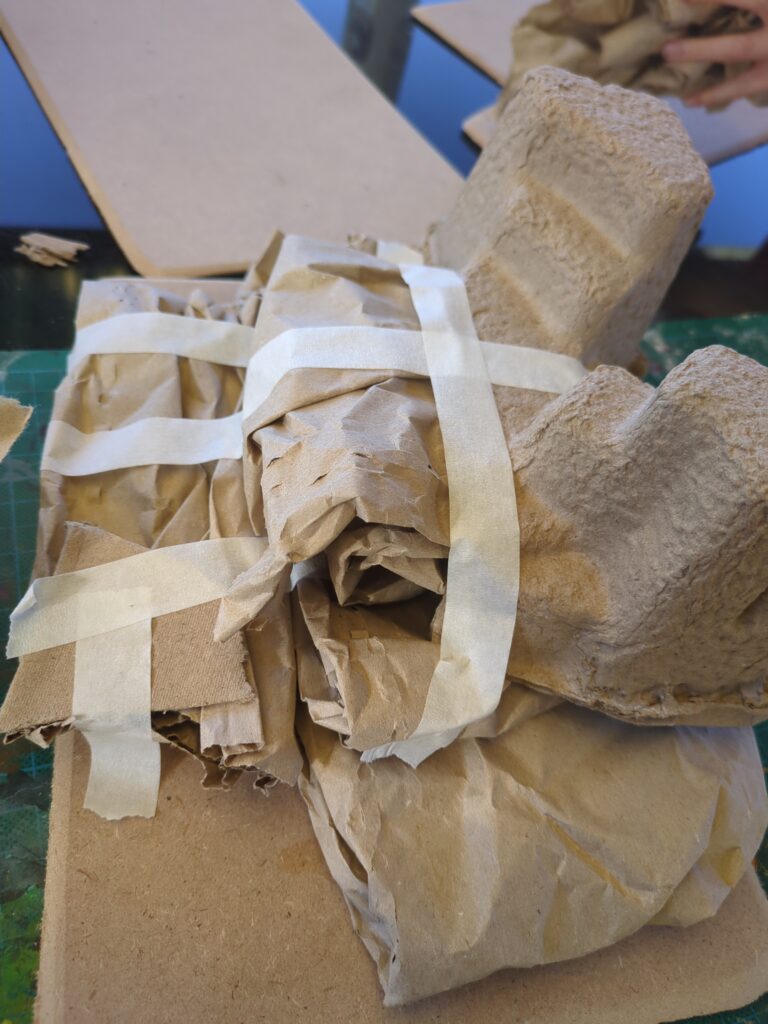 Several rolled up pieces of brown paper are stacked together and taped down with masking tape.
