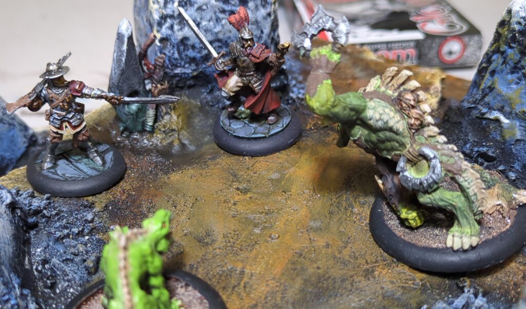 Two hell dorado conquistadors valiantly fight near an old cairn, as lizardmen attempt to drive them over a cliff.